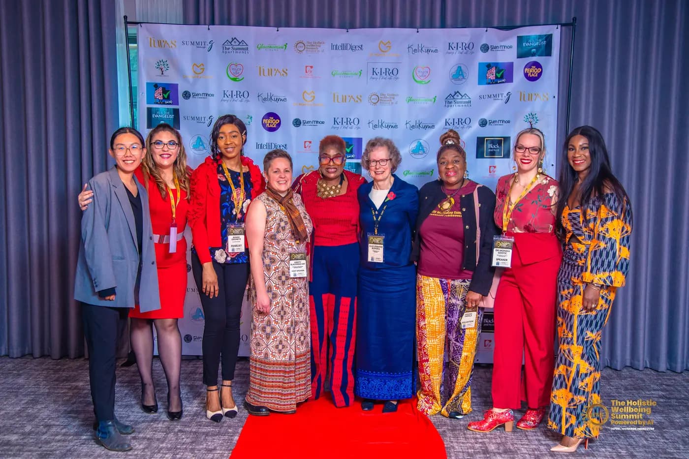 Speakers, panellists and volunteers standing together in front of the summit's sponsor board.