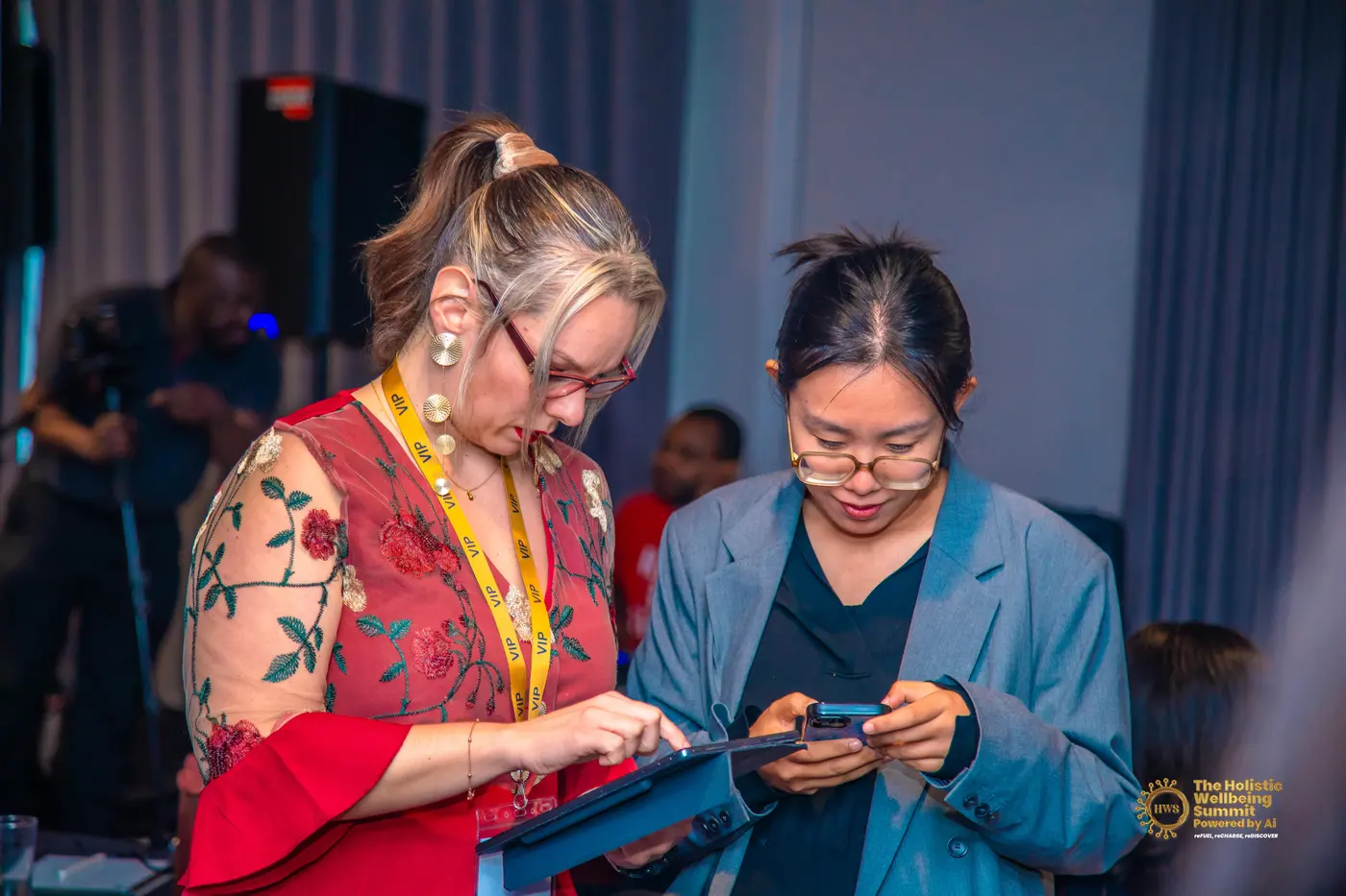 Two women comparing something on a tablet and a phone during the summit.